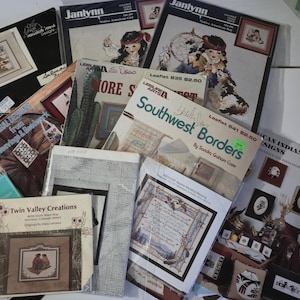 May include: A collection of cross-stitch patterns and leaflets, featuring designs with Native American themes, Southwestern borders, and other folk art motifs. The color palette includes earth tones, blues, and reds.