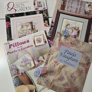 May include: A collection of Paula Vaughan cross-stitch and quilting books. Titles include "Quilts from the Garden," "A Mother's Love," "Pillows from Paula's Garden," and "Paula Vaughan In Miniature." The covers feature floral and domestic scenes.