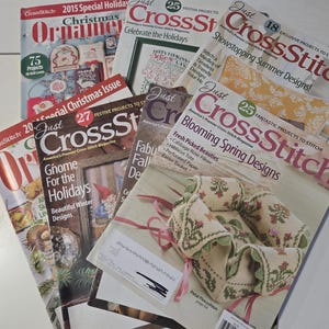 May include: A collection of Just CrossStitch magazines featuring various seasonal themes, including Christmas Ornaments, holiday gnomes, and spring designs. The covers display colorful cross-stitch projects, project counts, and titles like Blooming Spring Designs and Showstopping Summer Designs.