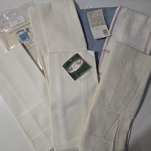 May include: A collection of various white and light-colored kitchen towels. Some towels have textured patterns, while others are smooth. One towel has a tag that reads "Terry Cross Stitch Towel" with an image of a horse-drawn carriage. Another tag reads "Crown Stitch Collectibles".