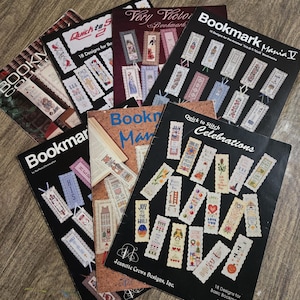 May include: A collection of bookmark design books, featuring various titles like "Bookmark Mania V" and "Quick to Stitch Celebrations." The covers display colorful cross-stitch patterns and text, with designs for holidays and everyday use.