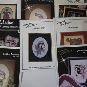 May include: A collection of Jeanne Christine cross-stitch pattern booklets. Titles include "Fantasy Mask," "The Elephant," and "Orchid Mask." The booklets feature framed cross-stitch designs with images of masks, animals, and other decorative elements.