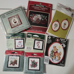May include: A collection of Christmas-themed counted cross-stitch kits. The kits feature various designs, including Santa Claus, a candy cane, a reindeer, and festive floral arrangements. The kits are packaged in various sizes and colors.