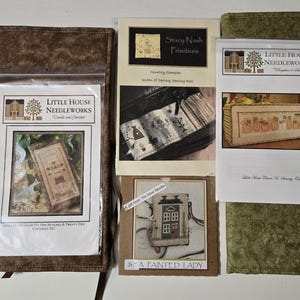 May include: A collection of cross-stitch patterns and accessories. The patterns include designs from Little House Needleworks, Stacy Nash Primitives, and A Painted Lady. The color palette includes brown, green, and cream.