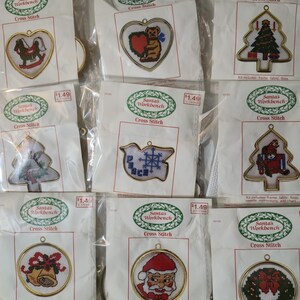 May include: A collection of Christmas cross-stitch kits from Santa's Workbench. The kits feature various holiday-themed designs, including a rocking horse, teddy bear with a heart, Christmas tree, and Santa Claus. Each kit includes a frame, fabric, and instructions.