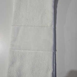 May include: Folded white towel with a textured waffle weave band. The towel is made of a soft, absorbent material, perfect for use in a bathroom or spa. The towel is clean and neatly folded.