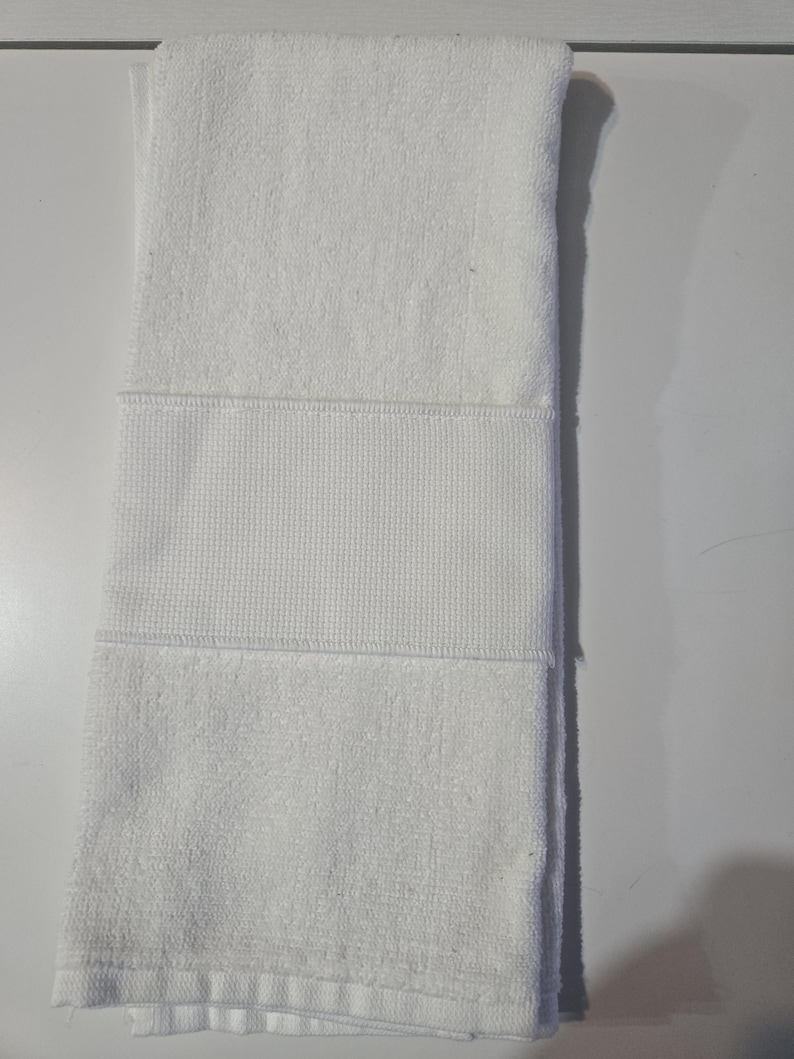 May include: Folded white towel with a textured waffle weave band. The towel is made of a soft, absorbent material, perfect for use in a bathroom or spa. The towel is clean and neatly folded.