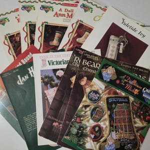 May include: A collection of Christmas-themed craft pattern booklets. The covers feature images of stockings, ornaments, and other holiday decorations. Titles include "A Doll Ann M", "Yuletide Ivy", and "Victorian".