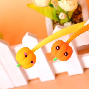 Può includere: Due porta cellulari a forma di zucca arancione con facce carine e steli verdi. I supporti sono attaccati a cavi flessibili gialli e arancioni.