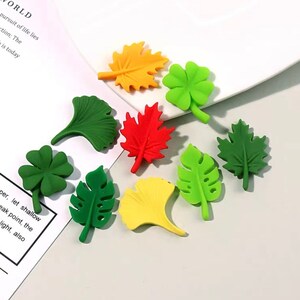 May include: Assortment of nine colourful plastic leaf shapes, including a maple leaf, a clover, a ginkgo leaf, and a monstera leaf.