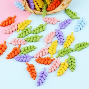 May include: Assortment of colorful plastic leaves in various shades of green, yellow, orange, pink, and purple. The leaves are scattered on a light blue surface.