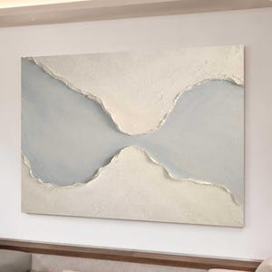 May include: A large rectangular abstract painting featuring thick, textured off-white impasto sections separated by a smooth, light gray central band with metallic silver edges. The text UniqueartworkByAnne is printed in black on the lower left.