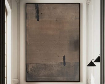 May include: A large rectangular abstract painting in shades of taupe, gray, and brown, featuring a dark vertical brushstroke near the top and a smaller one near the bottom, all enclosed within a thin black frame hanging on a white wall.