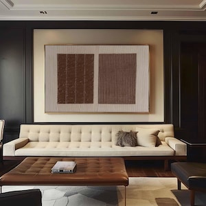 Puede incluir: Sal&oacute;n moderno con un sof&aacute; beige con mechones, una mesa de centro de cuero marr&oacute;n y una gran obra de arte abstracta. La obra de arte tiene dos cuadrados texturizados marrones y un fondo beige. La habitaci&oacute;n tiene detalles en madera oscura y una paleta de colores neutros.