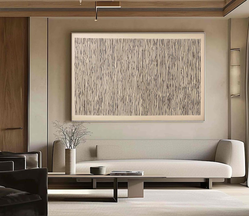 May include: A large, rectangular abstract artwork with a cream-colored background and vertical, textured lines in shades of brown and beige. The artwork is framed and hangs above a light-colored sofa. The room features neutral tones and minimalist decor.
