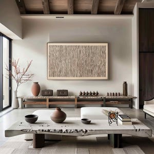 May include: A modern living room with neutral tones. A large, framed artwork with a vertical line pattern hangs above a wooden bench. Decorative vases, bowls, and small sculptures are arranged on the bench and a large, live-edge coffee table. The room has a minimalist aesthetic.