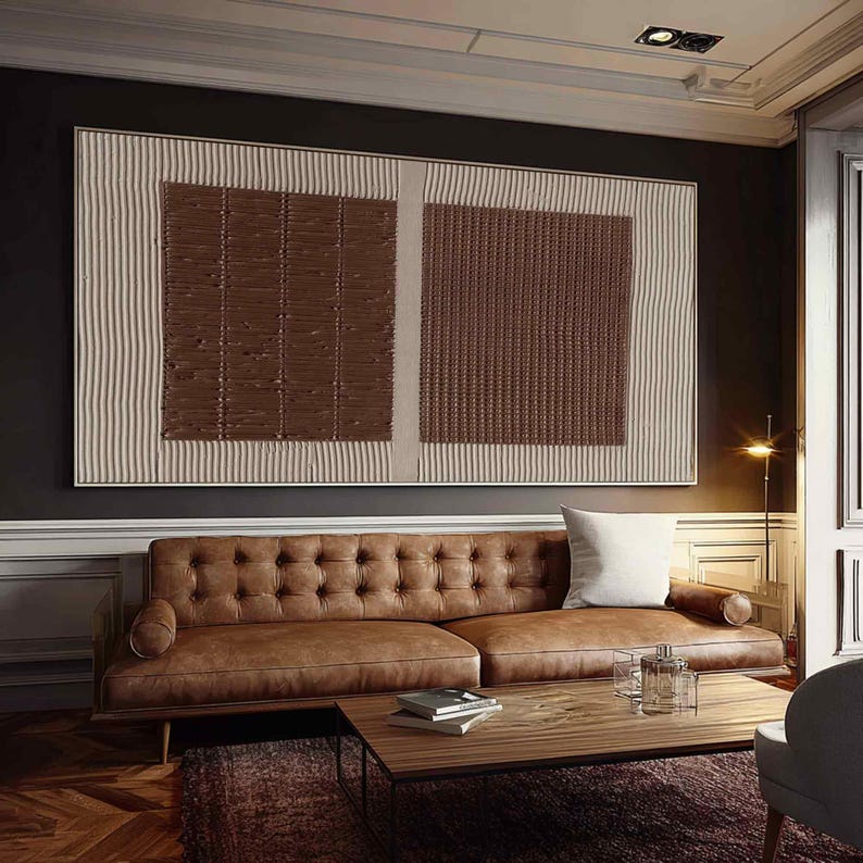 Puede incluir: Gran obra de arte mural abstracto con un dise&ntilde;o texturizado. La obra presenta dos cuadrados texturizados marrones sobre un fondo beige con rayas verticales. Un sof&aacute; de cuero marr&oacute;n y una mesa de centro de madera est&aacute;n frente a la obra.