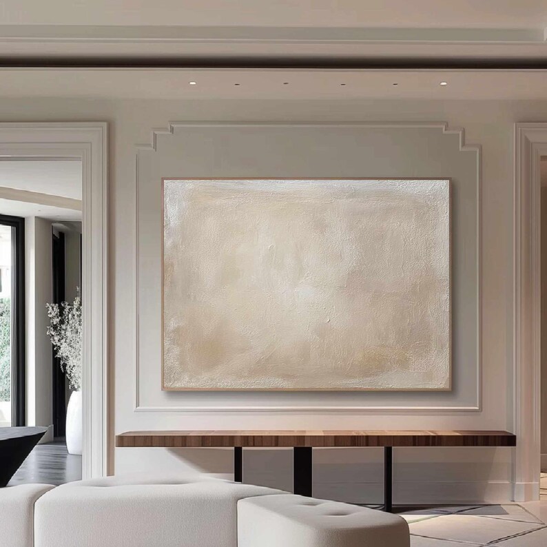 May include: Large abstract painting with a neutral color palette. The artwork features a textured surface with shades of beige and white, framed in a natural wood. The painting hangs above a dark wood console table.