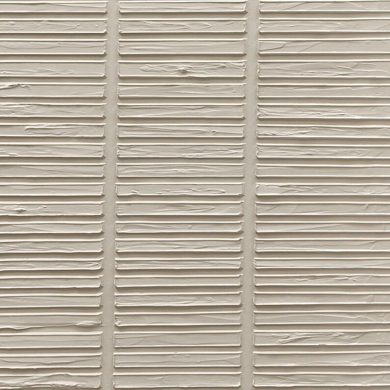 Puede incluir: Una pieza de arte mural texturizada que presenta una serie de barras rectangulares horizontales en relieve de color blanco roto, dispuestas en tres columnas verticales. La superficie muestra una aplicaci&oacute;n de pintura espesa y visible.