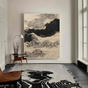 Puede incluir: Obra de arte abstracta con una paleta de colores neutros. La obra presenta un diseño texturizado en blanco y negro que recuerda a nubes u olas. La habitación también incluye una alfombra con un patrón similar, una silla de madera y una lámpara de pie.