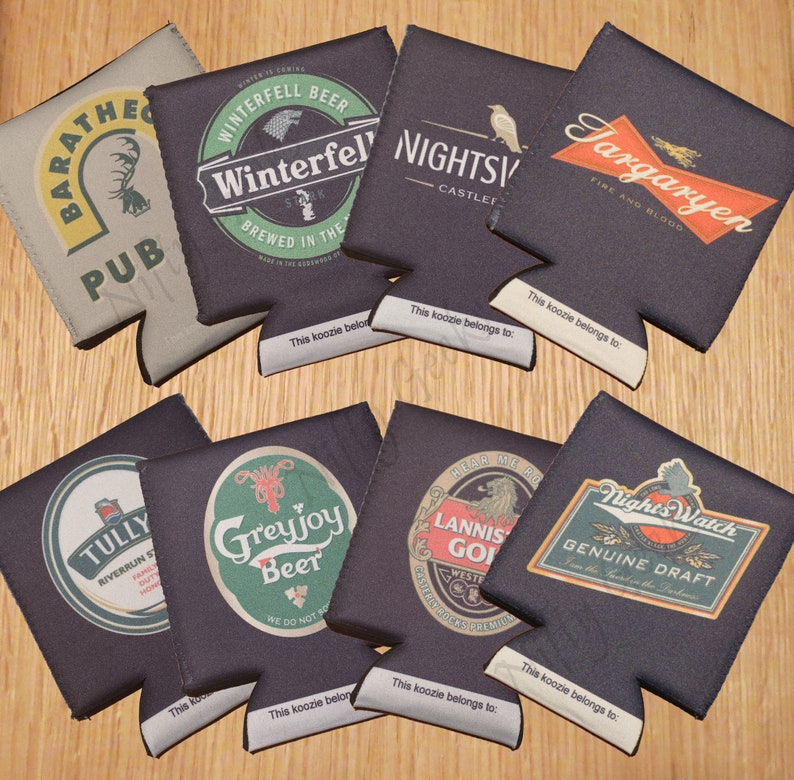 May include: Ten different koozies with various designs and text. The koozies are all black, brown, or gray with white text. The text includes the names of houses from the TV show Game of Thrones, such as Targaryen, Winterfell, and Greyjoy.