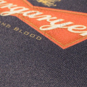 May include: A close-up of a navy blue fabric with the words "Fire and Blood" and "Stranger" in white lettering on a red background.