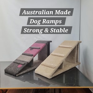 Puede incluir: Dos rampas para perros con superficies alfombradas. Una rampa es principalmente gris oscuro con un acento rosa, y la otra es beige. Las rampas tienen un dise&ntilde;o de escal&oacute;n y est&aacute;n etiquetadas como "Australian Made Dog Ramps Strong & Stable."