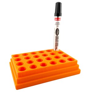 May include: An orange tiered pen holder with multiple circular openings, holding a black and white marker. The marker has the text "TESTORS" and "ENAMEL PAINT MARKER" printed on it. The pen holder is made of plastic.