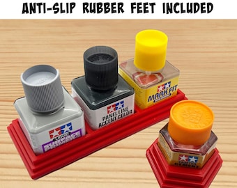 Op de afbeelding: Rode plastic organizer met vier vakken om kleine flesjes verf in te bewaren. De organizer heeft een antislip rubberen basis en een anti-kantel ontwerp. De flesjes zijn gelabeld met "Tamiya Liquid Surface Primer", "Tamiya Panel Line Accent Color", "Tamiya Mark Fit Decal Solution" en "Tamiya Cement".