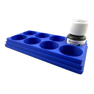 May include: A blue plastic paint organizer tray with six circular recessed slots for holding paint bottles. One small bottle of Humbrol Dark Green Wash with a white screw-top cap is placed inside one of the circular slots on the right side.