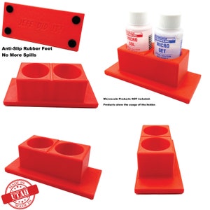May include: Red plastic holder with two round openings for bottles. The holder has a base and a raised section with the openings. The holder has anti-slip rubber feet on the bottom. The text "JEFF DID IT!" is embossed on the top of the holder. The text "Anti-Slip Rubber Feet No More Spills" is printed below the holder. The text "MADE IN UTAH MADE IN" is printed on a red circle on the base of the holder.