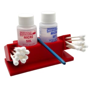 May include: A red plastic holder with two small bottles of setting solution for decals. The bottles are labeled "Microscale Industries, Inc." and have the text "Micro Sol" and "Micro Set" on them. The holder also includes a blue applicator stick and several cotton swabs.