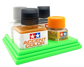 Op de afbeelding: Een groene plastic organizer met vier vakken om kleine flesjes verf in te bewaren. De flesjes zijn gelabeld met "Accent Color", "Tamiya Cement" en twee andere flesjes met onleesbare labels.