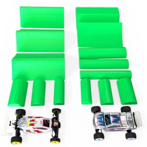 Può includere: Due piccole auto telecomandate con ruote nere e design colorati sono esposte. Le accompagnano diversi pezzi di schiuma verde brillante, rettangolari e cilindrici, probabilmente per la costruzione di piste o ostacoli. Le auto sono posizionate nella parte inferiore dell'immagine.