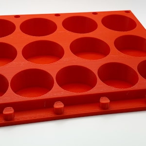 May include: Red silicone mold with 12 round cavities. The mold has a textured surface and is designed for making small cakes or other treats.