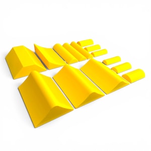 Puede incluir: Un conjunto de formas geométricas de color amarillo brillante, que incluyen prismas rectangulares, prismas triangulares y cilindros redondeados. Los objetos están dispuestos sobre una superficie blanca, creando una exhibición visualmente atractiva. Las formas varían en tamaño.