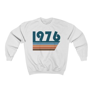 Può includere: Felpa bianca con un design retrò blu e marrone con l'anno 1976.