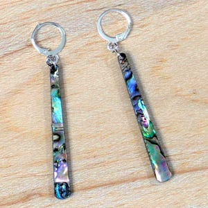 May include: A pair of dangle earrings with iridescent abalone shell inlays. The earrings have a silver-colored lever-back closure and a rectangular shape that tapers towards the bottom. The abalone shell displays a mix of blue, green, and purple hues.