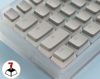 May include: Close-up of a mechanical keyboard with light gray keycaps and a white base. The keycaps have gray accents and various symbols and letters. The keyboard is set against a light blue background. The keys include "Esc", "Ctrl", "Alt", and number keys.