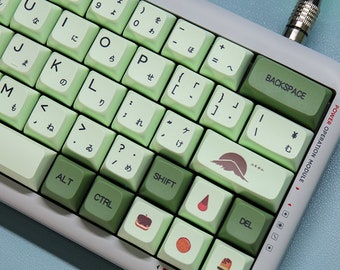 May include: A green and white keyboard with Japanese characters on the keys. The keyboard has a variety of keycaps with different designs, including a mountain, a strawberry, a donut, an orange, and a popsicle. The keyboard is connected to a green cable.