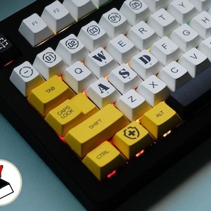 May include: A black mechanical keyboard with yellow and white keycaps. The keys are labeled with letters, numbers, and symbols. The keyboard has a black frame and a black base.