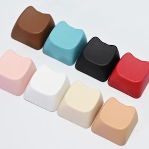 May include: Eight different colored keycaps with a cat ear design. The colors are brown, teal, black, red, pink, white, beige, and peach.