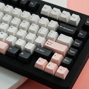 May include: A black mechanical keyboard with white and pink keycaps. The keyboard has a pink accent bar and black keys for function and navigation.