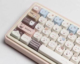 Könnte beinhalten: Eine rosa Tastatur mit weißen Tasten und benutzerdefinierten Tastenkappen mit niedlichen Katzenillustrationen. Die Tastenkappen sind in einem Pastellfarbschema mit braunen, rosa und blauen Akzenten gehalten. Die Tastatur hat eine Leertaste mit einem weißen und rosa Design.