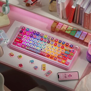 May include: A pink keyboard with rainbow colored keys and a colorful design. The keyboard has the words "MUSIC FESTIVAL" printed on it. The keyboard is surrounded by other colorful objects, including a pink desk, a xylophone, and a phone.