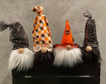 May include: Four Halloween gnomes with different hats. The gnomes have white beards and black hair. The hats are black and orange with spiderwebs and a spider.