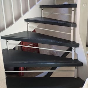 Puede incluir: Una escalera interior con peldaños triangulares de color gris carbón oscuro y barandillas de metal blanco. El diseño de la escalera incluye un zanca lateral blanca y balaustres verticales blancos que conectan cada escalón, creando una estructura geométrica.