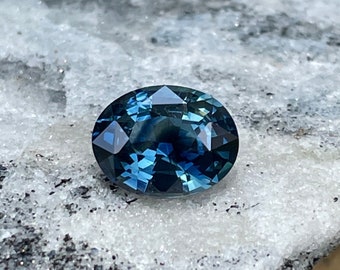 May include: A deep blue oval-shaped sapphire gemstone with a faceted cut. The gemstone is set against a white background.