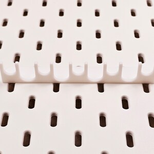 May include: White plastic pegboard organizer with nine hooks. The organizer is designed to hang on a pegboard wall.