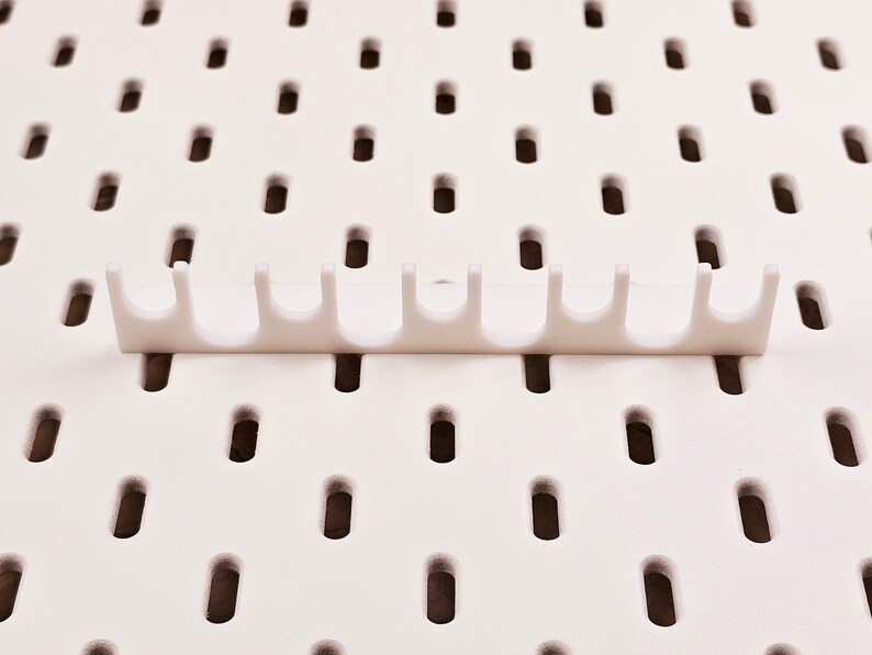 May include: White plastic pegboard organizer with nine hooks. The organizer is designed to hang on a pegboard wall.